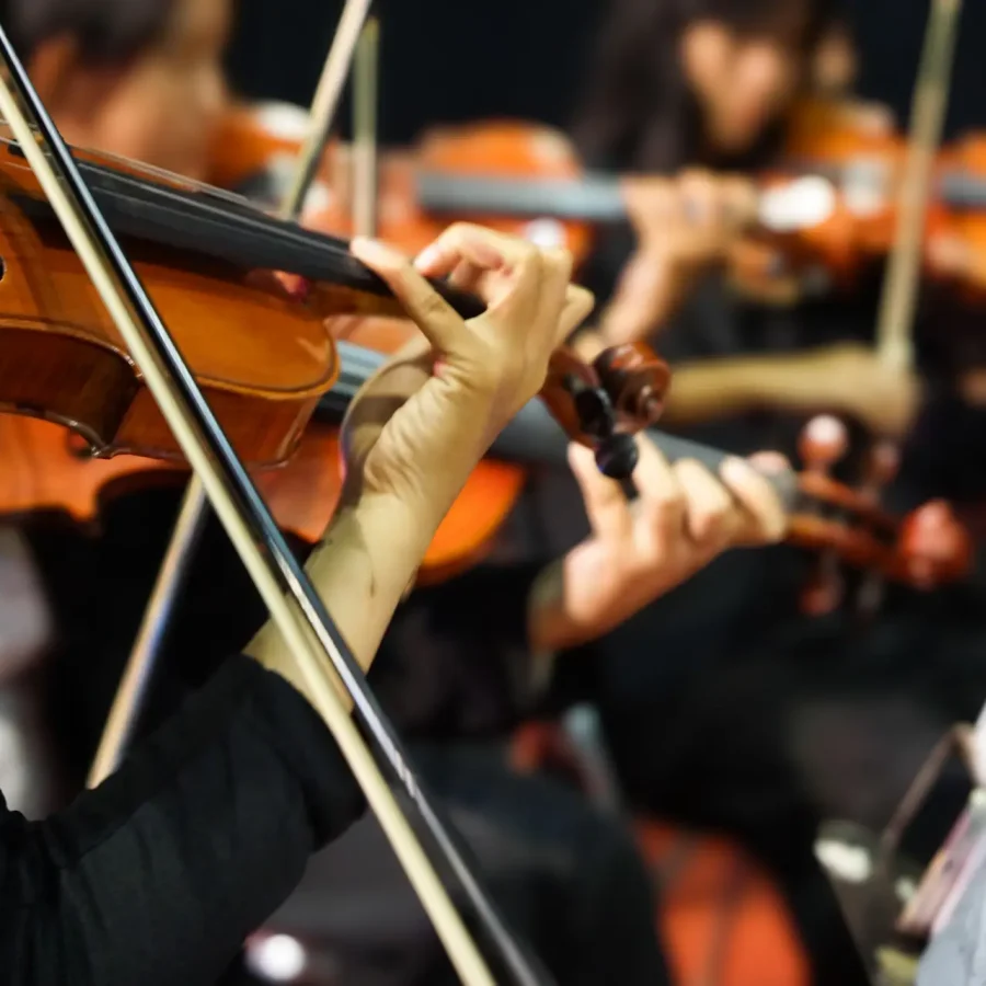 Hands playing violin orchestra with note sheet on stage.